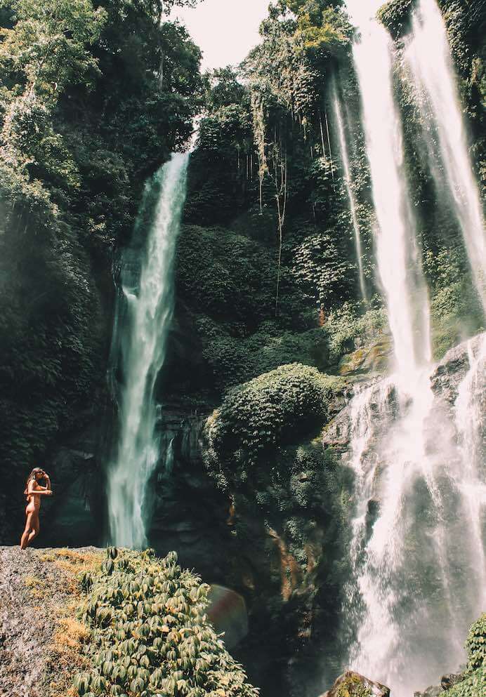 solo vacation - girl standing under waterfall in bali