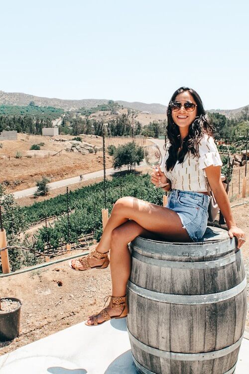 travel - picture of girl sitting on barrel drinking wine overlooking a vineyard