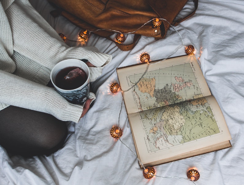 plan solo trip - girl sitting in bed drinking tea looking at a map of the world