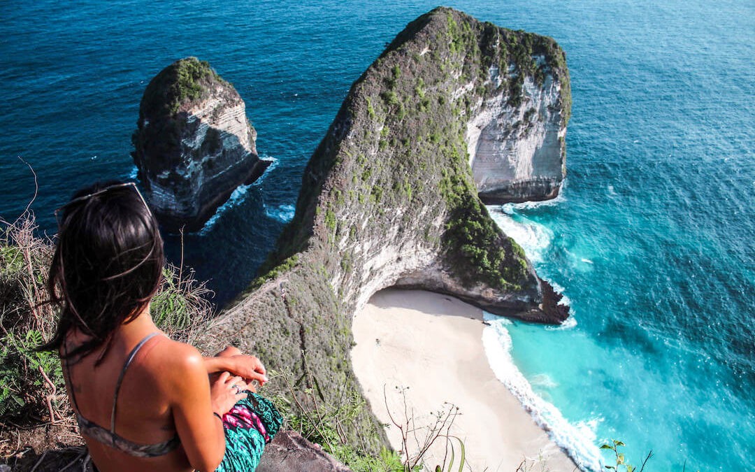 travel to bali - girl sitting on cliff overlooking kelingking beach nusa penida bali