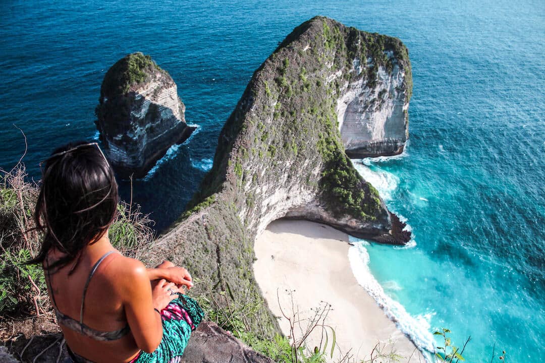 travel to bali - girl sitting on cliff overlooking kelingking beach nusa penida bali